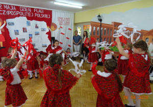 Na tle dekoracji z mapą Polski i dziećmi z chorągiewkami tańczą dziewczynki przebrane za góralki.